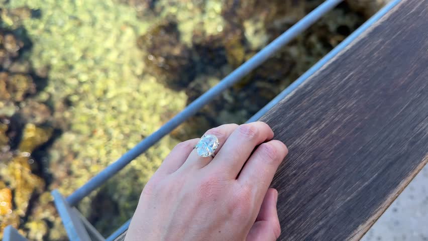 A landscape view of a hand with an engagement ring by the Adriatic coast, showing turquoise water, sunlight and Mediterranean atmosphere.