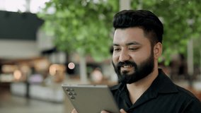 Portrait of bearded Indian man manager uses digital tablet in office building lobby. South Asian entrepreneur reads messages in online chat on mobile device in shopping mall - Powered by Shutterstock - Get 15% off with code: PIKWIZARD15