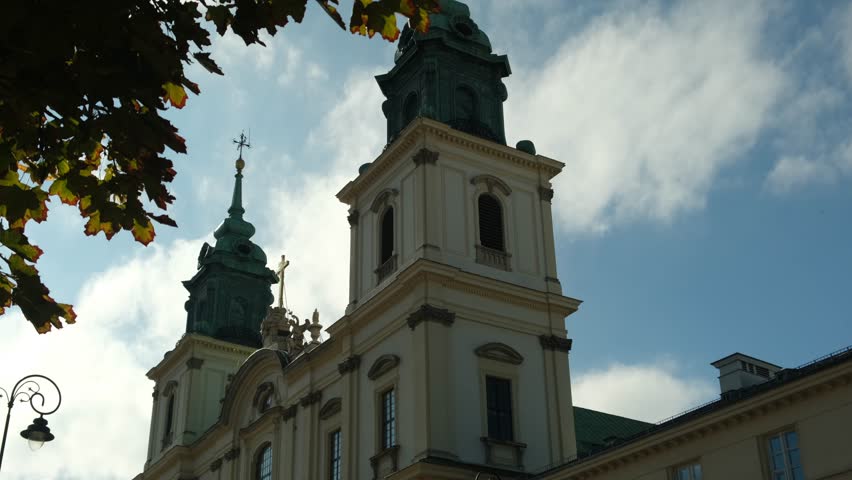 The stunning architecture of a church tower is highlighted against a bright blue sky with fluffy clouds. The sunlight enhances the details of the building in Warsaw, Poland.