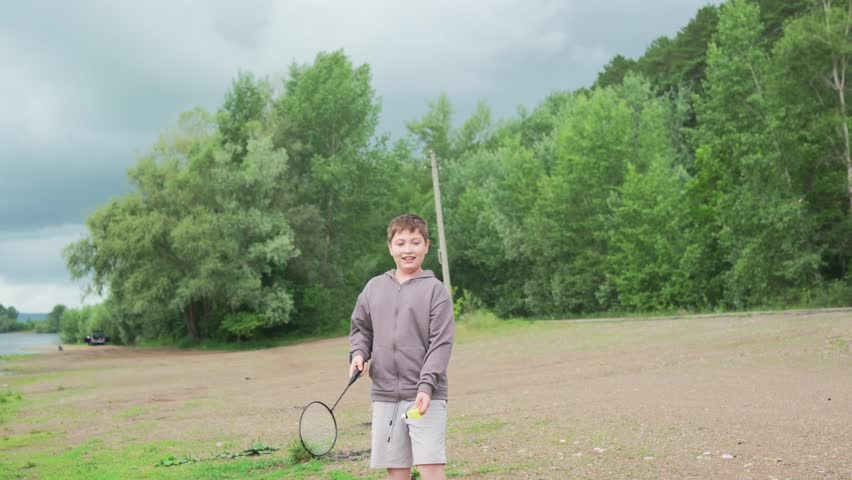 teen boy playing, young male athlete practicing badminton amidst lush trees and water