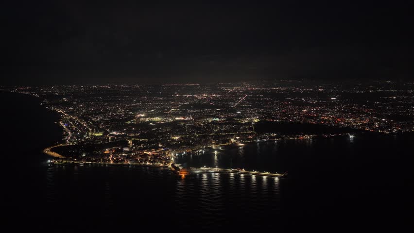Cinematic drone footage of Anzio city and coastline illuminated at night. Aerial view of Italian seaside town with reflections of urban lights over the sea.