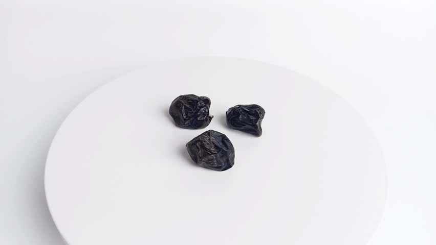 Three Ajwa dates rotating on a white podium with clean background. Minimalist healthy food concept symbolizing Ramadan nutrition and natural sweetness.
