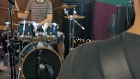 A drummer plays with concentration in a music studio. Soundproofing panels and other band equipment create a creative atmosphere. View from over the shoulder of the guitarist in the foreground - Powered by Shutterstock - Get 15% off with code: PIKWIZARD15