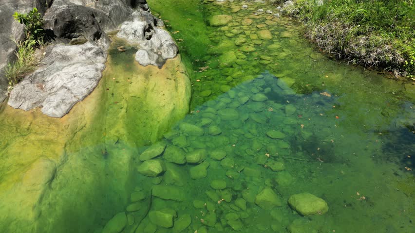 Aerial 4K view of Dos Aguas lagoon edges where clear water laps mossy rock formations