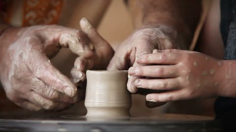 Hands of old potter and young pupil