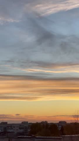 Vibrant sunset or sunrise over a dark city skyline. The sky is a beautiful gradient of deep blue, orange, and gold with soft clouds.