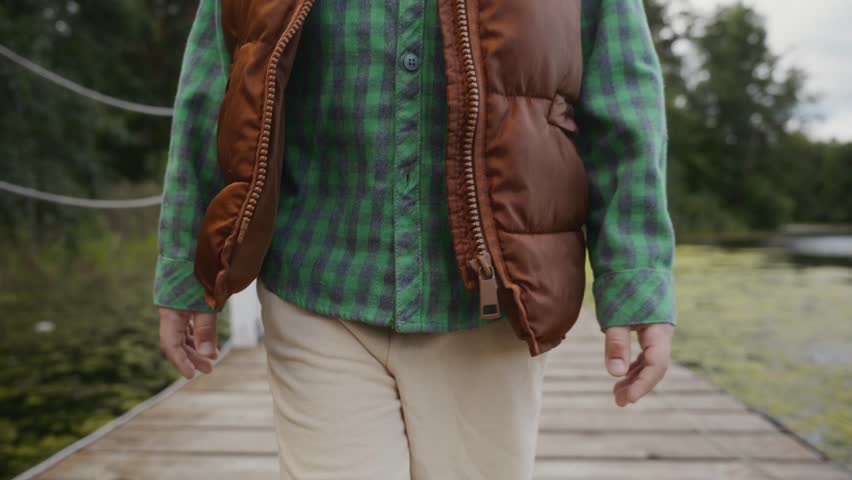 Medium close-up of boy in vest and shirt walking on pier. Symbolizes healthy lifestyle, balance and natural connection. High quality 4k footage