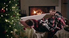 Two teenage girls fall asleep together on a cozy sofa under a checkered blanket, with a Christmas tree glowing softly beside them and a warm fire burning in the fireplace. High quality 4k footage - Powered by Shutterstock - Get 15% off with code: PIKWIZARD15