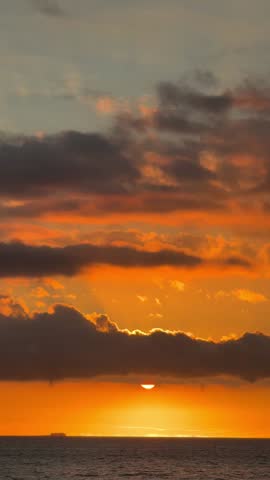 Fiery orange sunset over Tenerife ocean, sun sinking behind clouds, casting vibrant reflections on water. Cinematic aerial view capturing tropical coastal beauty and dramatic skies
