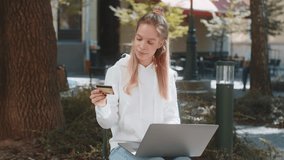 Smiling woman using credit card and laptop while transferring money, purchases online shopping, order food delivery, booking hotel room outdoors. Young teenager girl sitting in park city street. - Powered by Shutterstock - Get 15% off with code: PIKWIZARD15