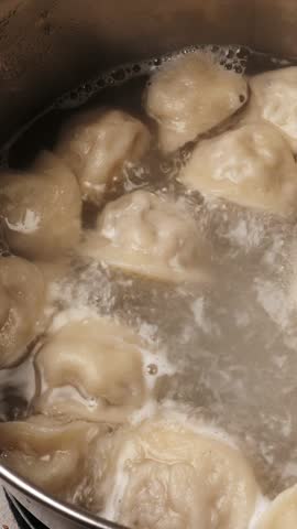 Boiling homemade meat dumplings, closeup. Cooking Russian traditional meal. Vertical footage