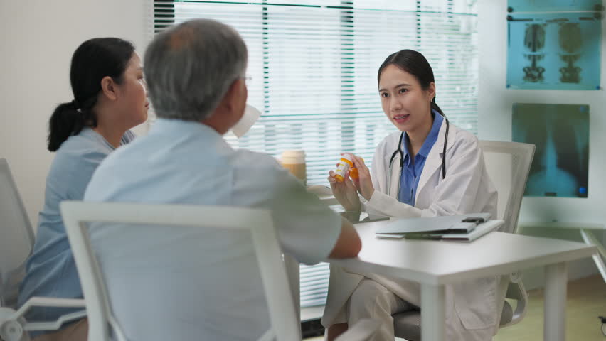 Asian female doctor explains how to take prescription medicine to elderly couple during a medical consultation in a modern clinic. Senior healthcare and patient care at hospital concept.