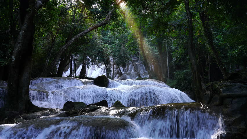 Tropical waterfall in lush forest illuminated by sunbeam, creating a magical and tranquil atmosphere. Perfect for nature inspiration, wellness visuals, eco-tourism, and meditation content.