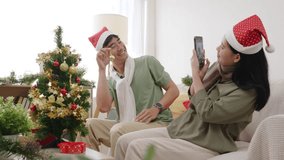 Happy christmas couple enjoying xmas holiday at home, people relaxing on couch near tree, presents waiting, woman takes video call, man laughs holding ornament, celebrating festive season together. - Powered by Shutterstock - Get 15% off with code: PIKWIZARD15