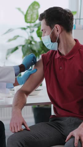 Young caucasian male patient visiting doctor for vaccoination process. Doctor pharmacist analyzing young man injecting vaccine against coronavirus.
