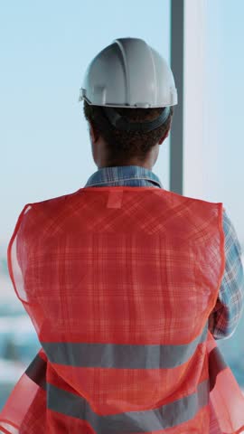 Back of professional foreman african american architect standing by large panoramic window observing cuityscape view with civil constructions.