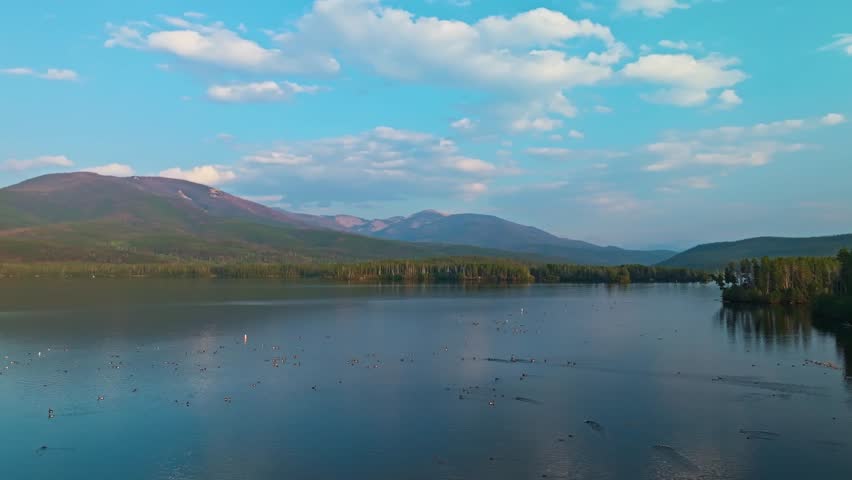 Drone orbits above wide blue Grand Lake Colorado with distant hills and pine forests under soft sunlight