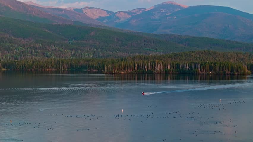 Drone orbit around boat racing across Grand Lake Colorado as twilight colors reflect on water