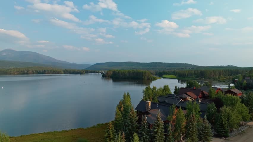 Drone aerial ascend over calm Grand Lake Colorado reflecting clouds and surrounding pine forest in early light, suburban homes on lakefront