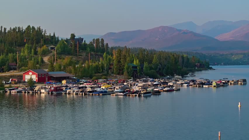 Drone orbit of boats anchored near shore and reflections across Grand Lake Colorado surrounded by green hills