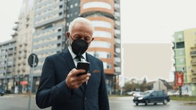 Successful senior businessman wearing a protective face mask walking on a city street and answering a phone call during the coronavirus pandemic, with urban traffic in the background - Powered by Shutterstock - Get 15% off with code: PIKWIZARD15