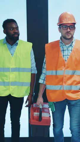 Two hardworking construction workers wearing appropriate safety gear and carrying a toolbox