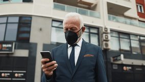 Successful senior businessman wearing a protective face mask walking on a city street and answering a phone call during the coronavirus pandemic, with urban traffic in the background - Powered by Shutterstock - Get 15% off with code: PIKWIZARD15