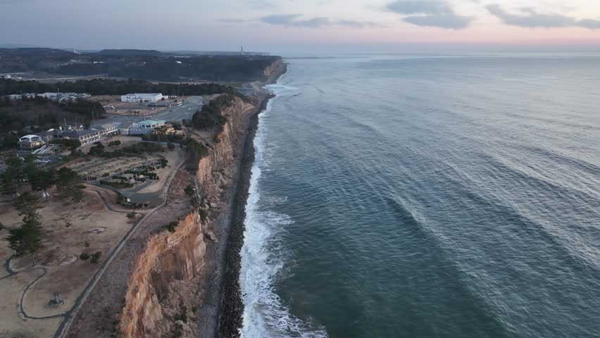 Cinematic drone footage over Japan’s coastline before sunrise. Flying between rugged cliffs and the Pacific Ocean, the scene glows softly with pre-dawn light, evoking calm and natural beauty.