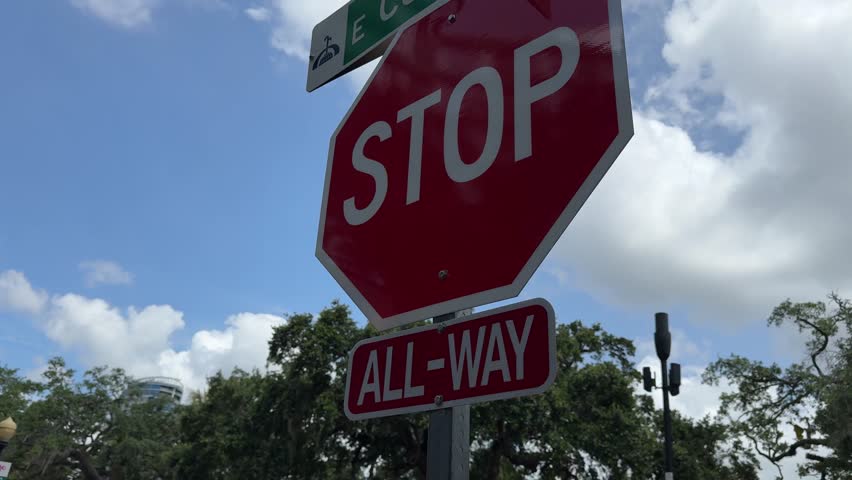 TILT SLOW MOTION SHOT - Orlando Road Sign in downtown Orlando, Florida, USA. Traffic signs STOP, red and white "All-way" sign. Direction sign to E Central Blvd and Lake Eola.