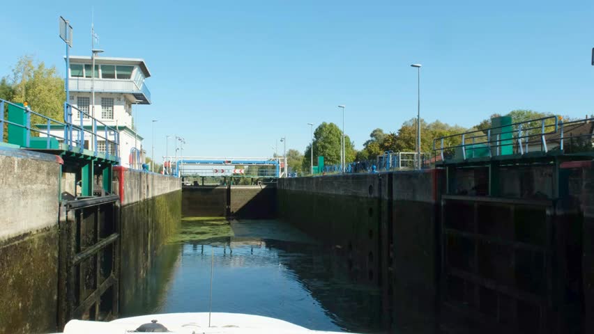 Lock 6 Pont Malin on Escaut canal with concrete walls, blue railing, calm water, and control building in a green riverside landscape. The water level is dropping.