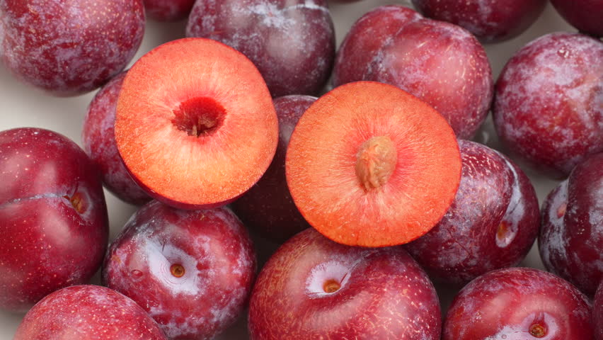 Top-down shot of fresh whole and half red plums spinning on a wooden board. Seamless loop. Healthy food background, fruit pattern, vitamin concept.
