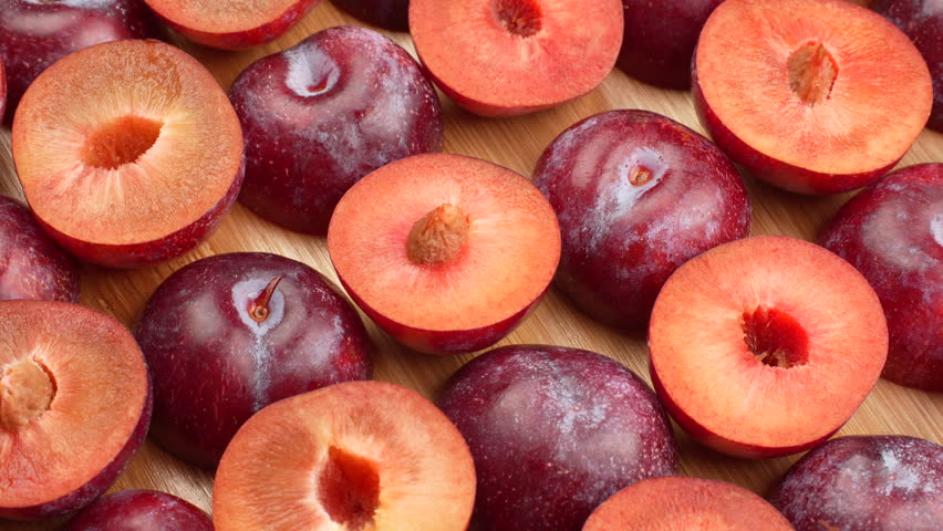 Top-down shot of fresh whole and half red plums spinning on a wooden board. Seamless loop. Healthy food background, fruit pattern, vitamin concept.