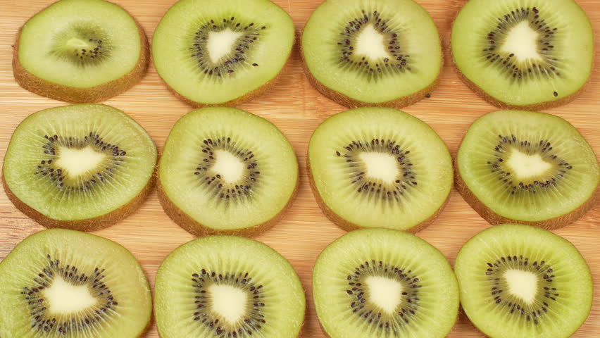 Static top-down shot of fresh green kiwi slices arranged in a neat pattern on a wooden cutting board. Healthy food background, vitamin C, and diet concept.