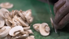 Close-up of sliced mushrooms on a cutting board with a hand in a glove chopping them. The green surface reflects a kitchen environment. Ideal for cooking or culinary themes. - Powered by Shutterstock - Get 15% off with code: PIKWIZARD15