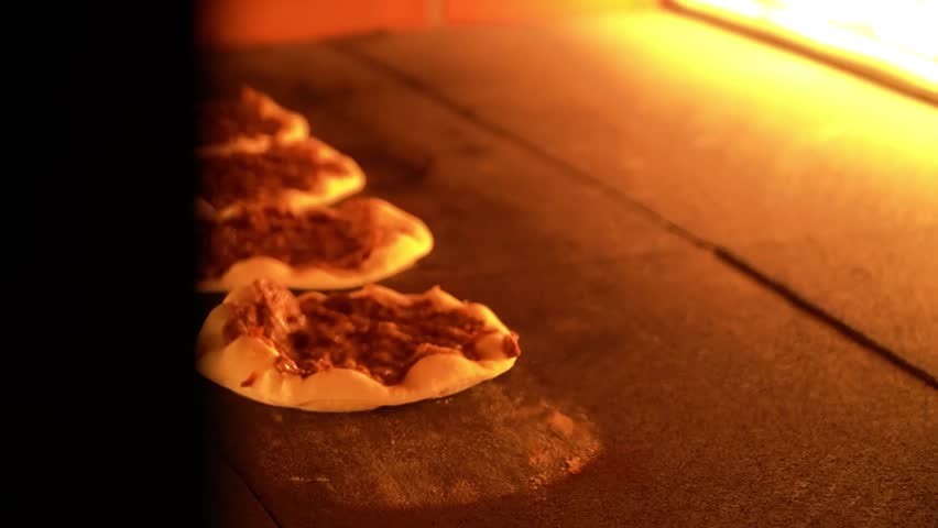 Freshly prepared bread being baked in a traditional oven, showcasing a close-up of the dough with toppings. The warm glow of the oven enhances the ambiance.