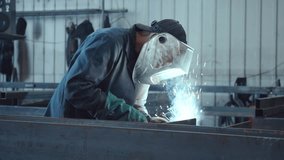 Industrial welder wearing a protective mask joining heavy metal parts with an arc welding machine, creating bright sparks and smoke in a metal fabrication workshop or factory - Powered by Shutterstock - Get 15% off with code: PIKWIZARD15