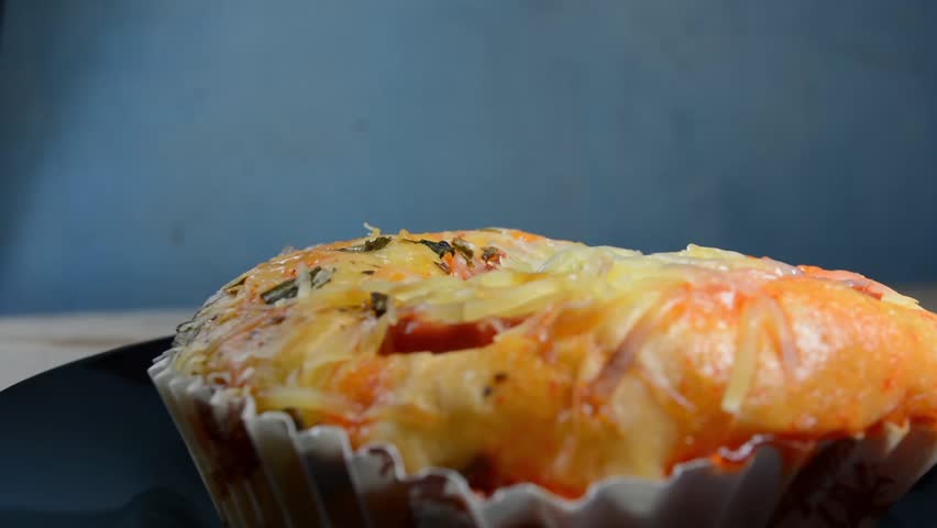 Delicious close-up of a savory bakery bun, likely a pizza bread, topped with shredded cheese, chili sauce, and fresh chopped green onions