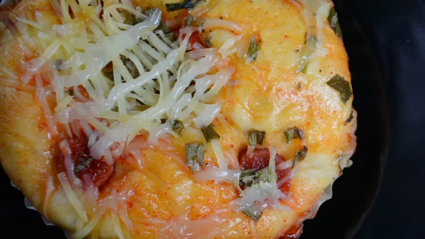 Delicious close-up of a savory bakery bun, likely a pizza bread, topped with shredded cheese, chili sauce, and fresh chopped green onions