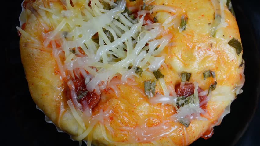 Delicious close-up of a savory bakery bun, likely a pizza bread, topped with shredded cheese, chili sauce, and fresh chopped green onions
