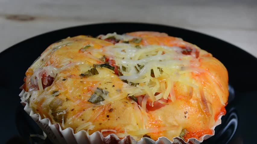 Delicious close-up of a savory bakery bun, likely a pizza bread, topped with shredded cheese, chili sauce, and fresh chopped green onions