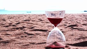 A clear hourglass symbolizes time passing as fine brown sand runs, resting on a beach with the vast, endless ocean and horizon in the background. - Powered by Shutterstock - Get 15% off with code: PIKWIZARD15