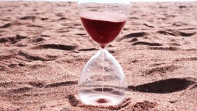 A clear hourglass symbolizes time passing as fine brown sand runs, resting on a beach with the vast, endless ocean and horizon in the background. - Powered by Shutterstock - Get 15% off with code: PIKWIZARD15
