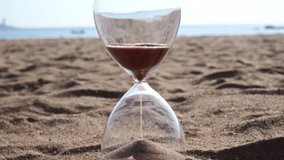 A clear hourglass symbolizes time passing as fine brown sand runs, resting on a beach with the vast, endless ocean and horizon in the background. - Powered by Shutterstock - Get 15% off with code: PIKWIZARD15