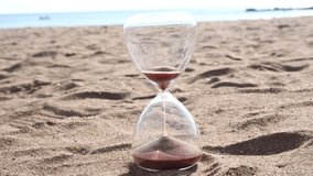 A clear hourglass symbolizes time passing as fine brown sand runs, resting on a beach with the vast, endless ocean and horizon in the background. - Powered by Shutterstock - Get 15% off with code: PIKWIZARD15