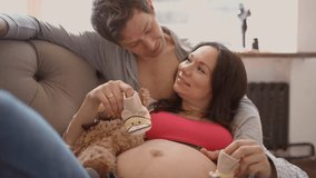 Expecting couple at home lying on sofa, husband gently plays with tiny baby shoes on wifes pregnant belly. - Powered by Shutterstock - Get 15% off with code: PIKWIZARD15