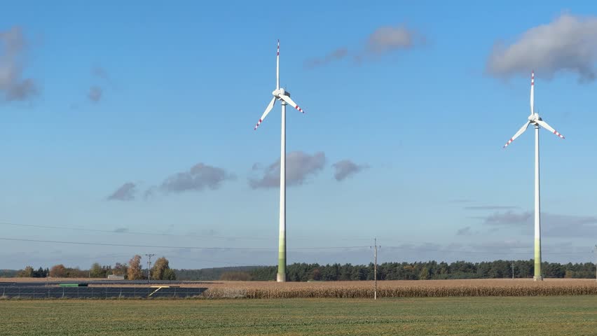 A cinematic hero shot panning video of wind turbines moving from left to right across a bright sky. The composition highlights renewable energy and environmental awareness.