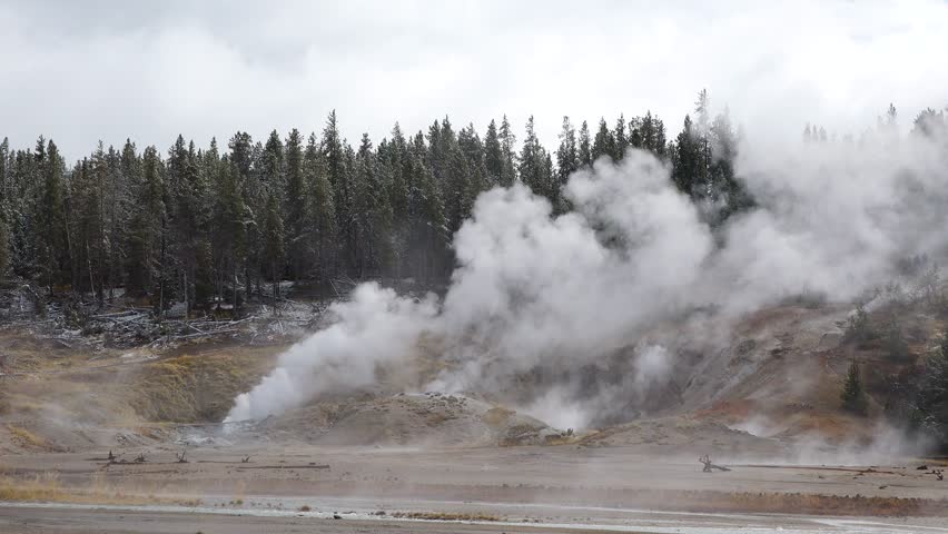 Geysers and steam rise in Yellowstone National Park during a cloudy day