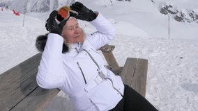 Woman in white ski jacket sunbathing on wooden bench after lunch at snow mountain resort. Removing goggles to relax and enjoy sunshine after day of skiing. Skier charged energy sun by closing eyes - Powered by Shutterstock - Get 15% off with code: PIKWIZARD15