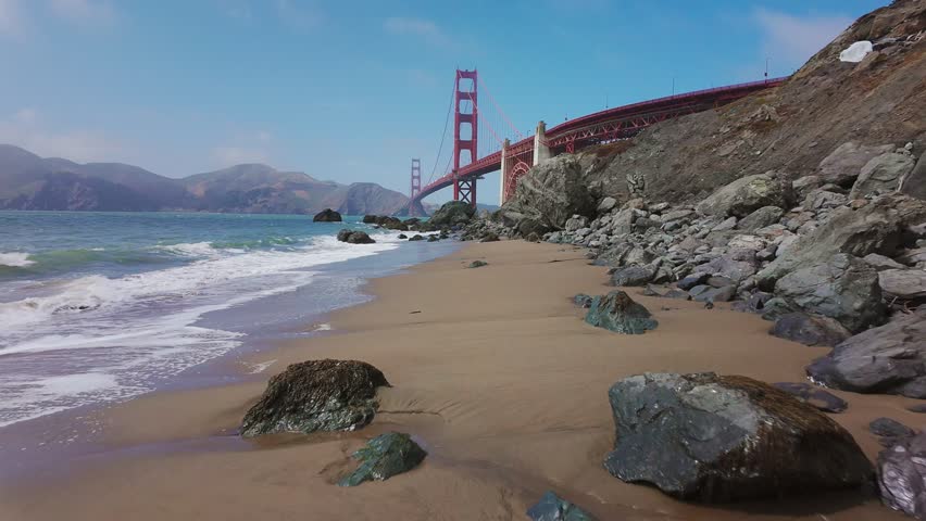 Waves roll onto sandy shore at Baker Beach with Golden Gate Bridge in background, San Francisco, California, USA. Iconic coastal view with ocean, rocks and Marin Headlands