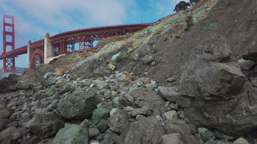 Waves roll onto sandy shore at Baker Beach with Golden Gate Bridge in background, San Francisco, California, USA. Iconic coastal view with ocean, rocks and Marin Headlands